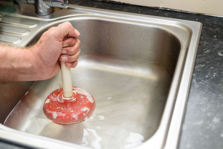 En mand bruger en svupper til at rense en køkkenhåndvask og yde kloakservice